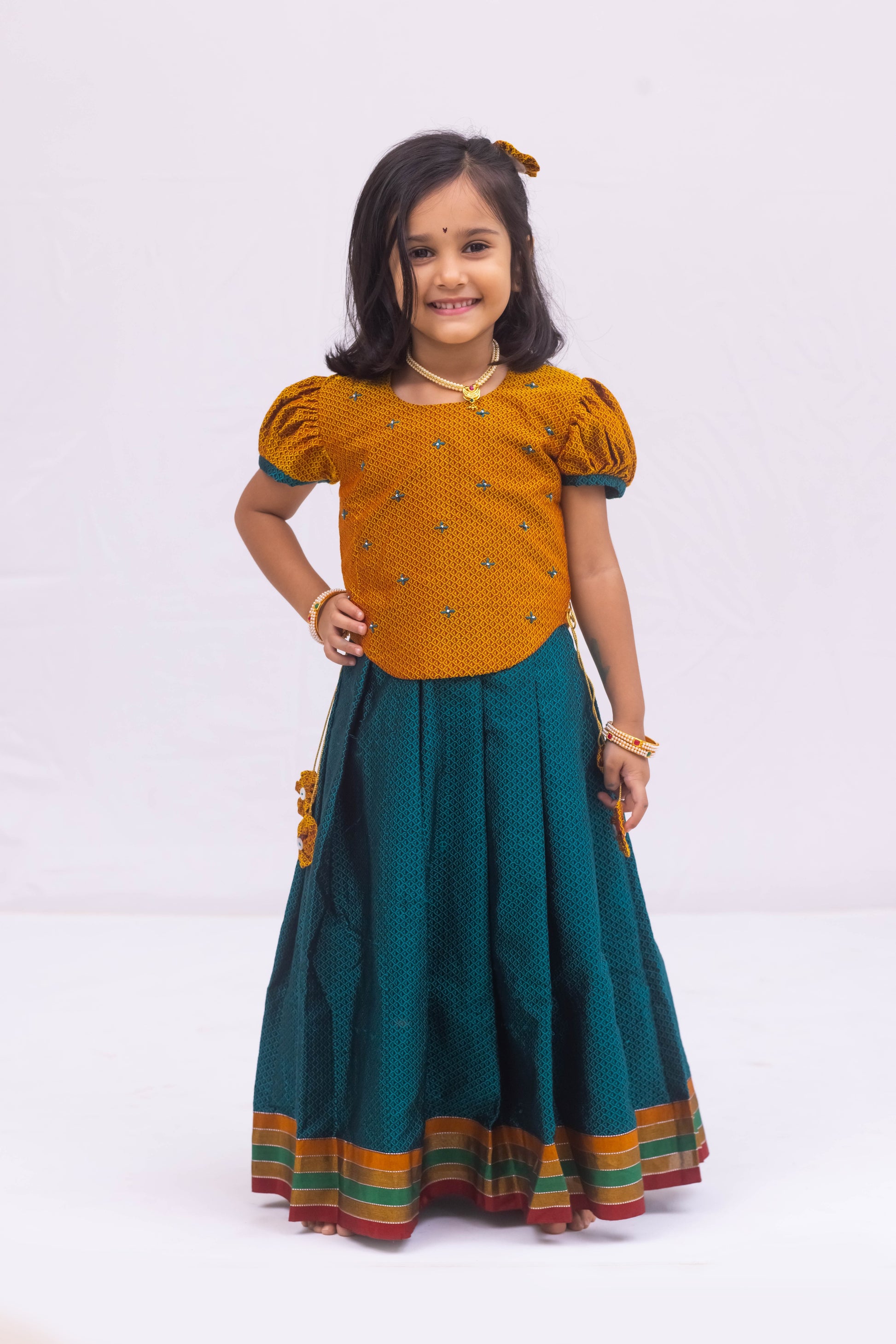 Peacock Green Khunn Dress with Contrast Turmeric Yellow hand embroidered blouse with cute puff sleeves. Apple cut blouse has cute flower latkans on both sides that dangle while walking. Also Unique Patti border of khunn is something not to miss for Khunn lovers