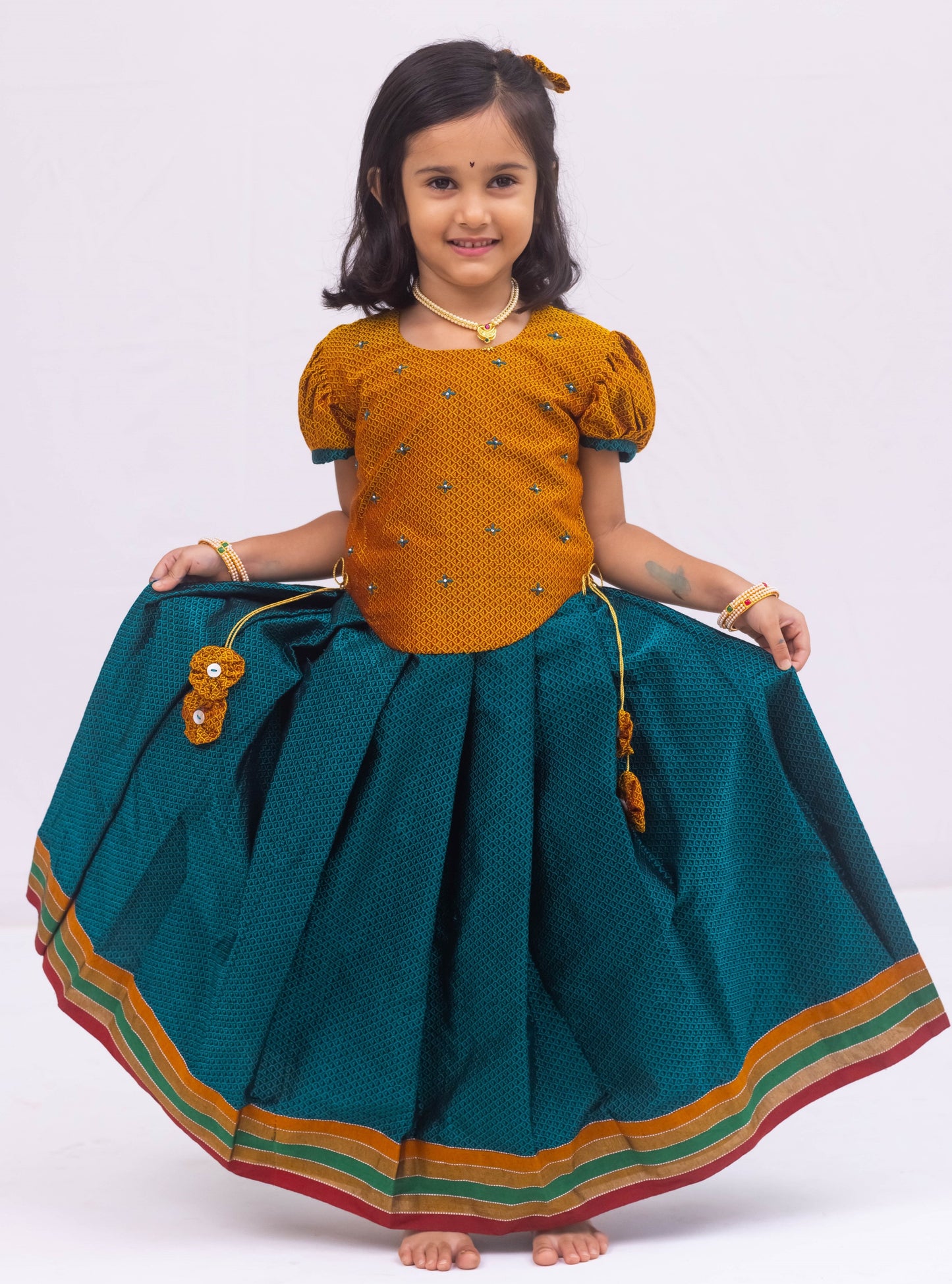 Peacock Green Khunn Dress with Contrast Turmeric Yellow hand embroidered blouse with cute puff sleeves. Apple cut blouse has cute flower latkans on both sides that dangle while walking. Also Unique Patti border of khunn is something not to miss for Khunn lovers