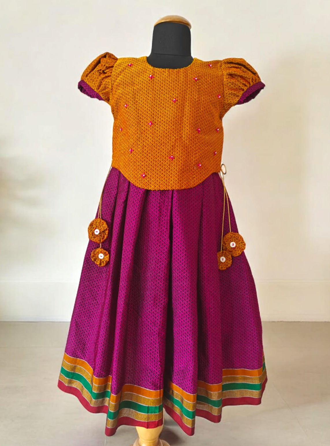 Magenta Khunn Dress with Contrast Turmeric Yellow hand embroidered blouse with cute puff sleeves. Apple cut blouse has cute flower latkans on both sides that dangle while walking. Also Unique Patti border of khunn is something not to miss for Khunn lovers