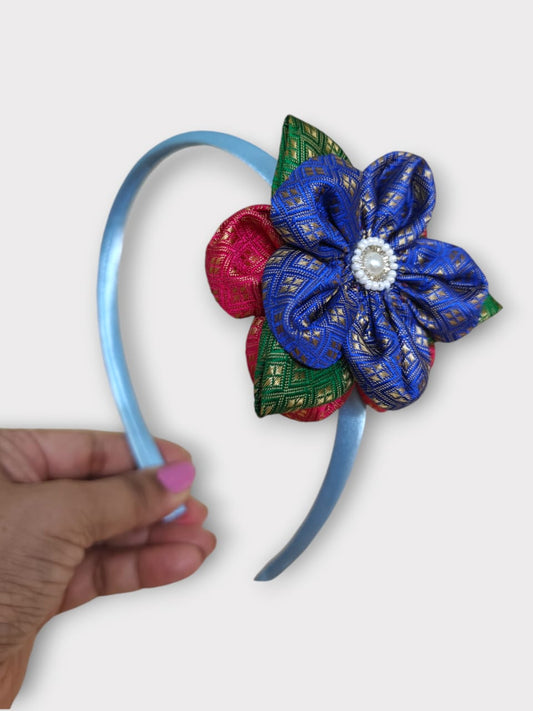 Blue brocade layered flower motif , satin wrapped plastic hairband for Girls.This blue brocade hairband features a layered flower motif and is wrapped in satin-covered plastic. It is perfect for girls aged two and up, making it a charming accessory for any outfit.
